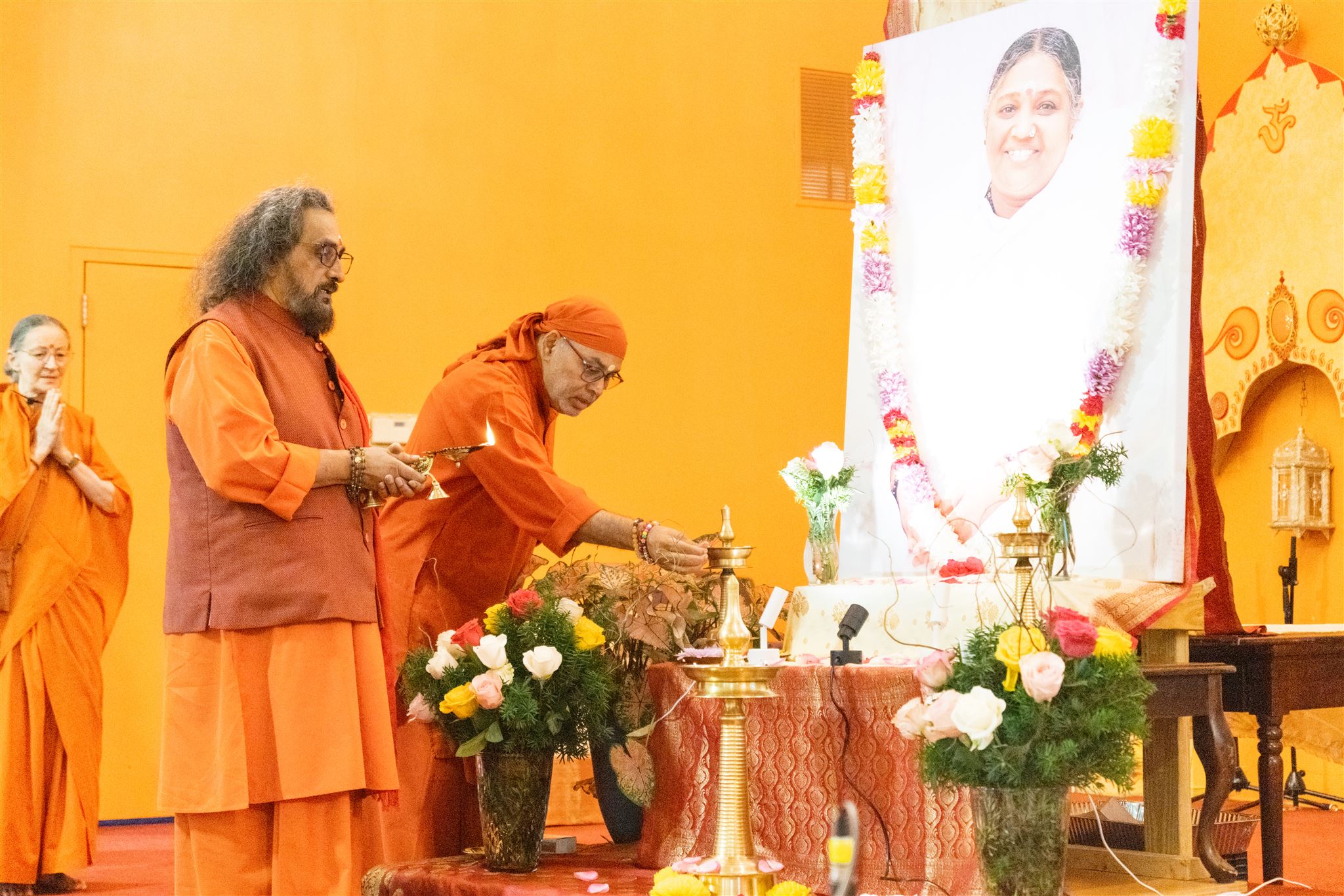 Swamis lighting a lamp before Amma’s portrait