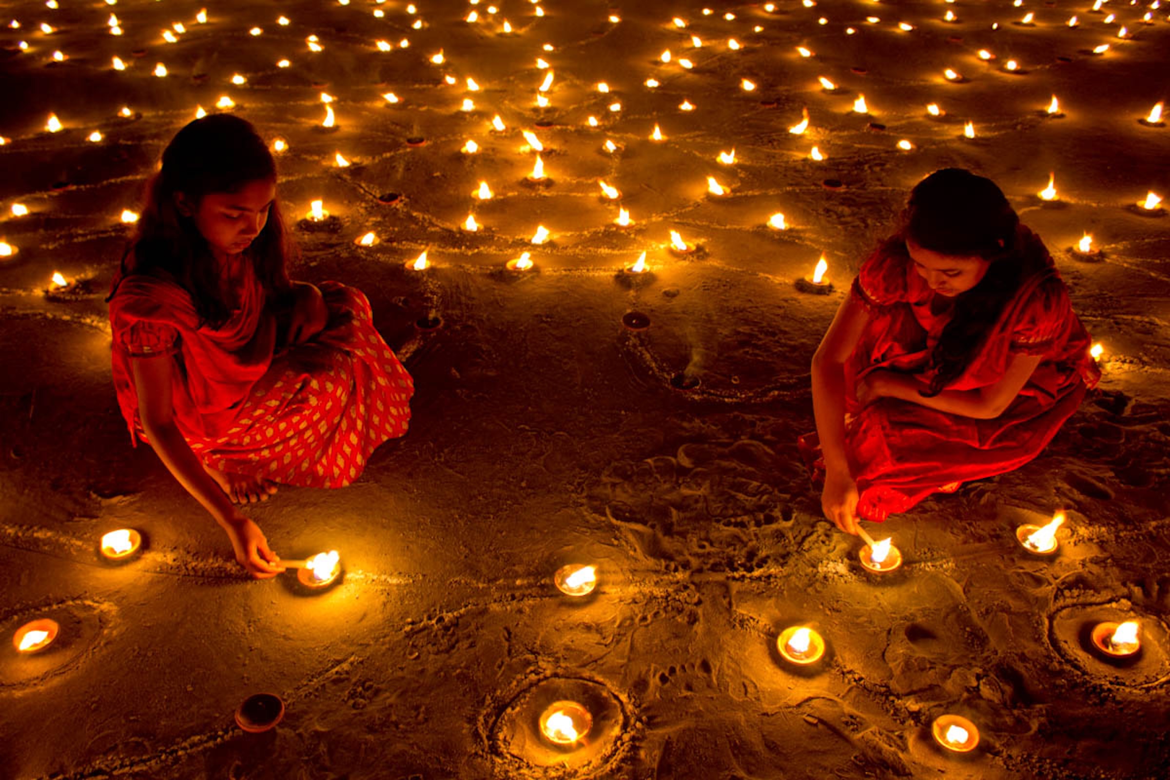 Girls lighting small clay lamps in the sand