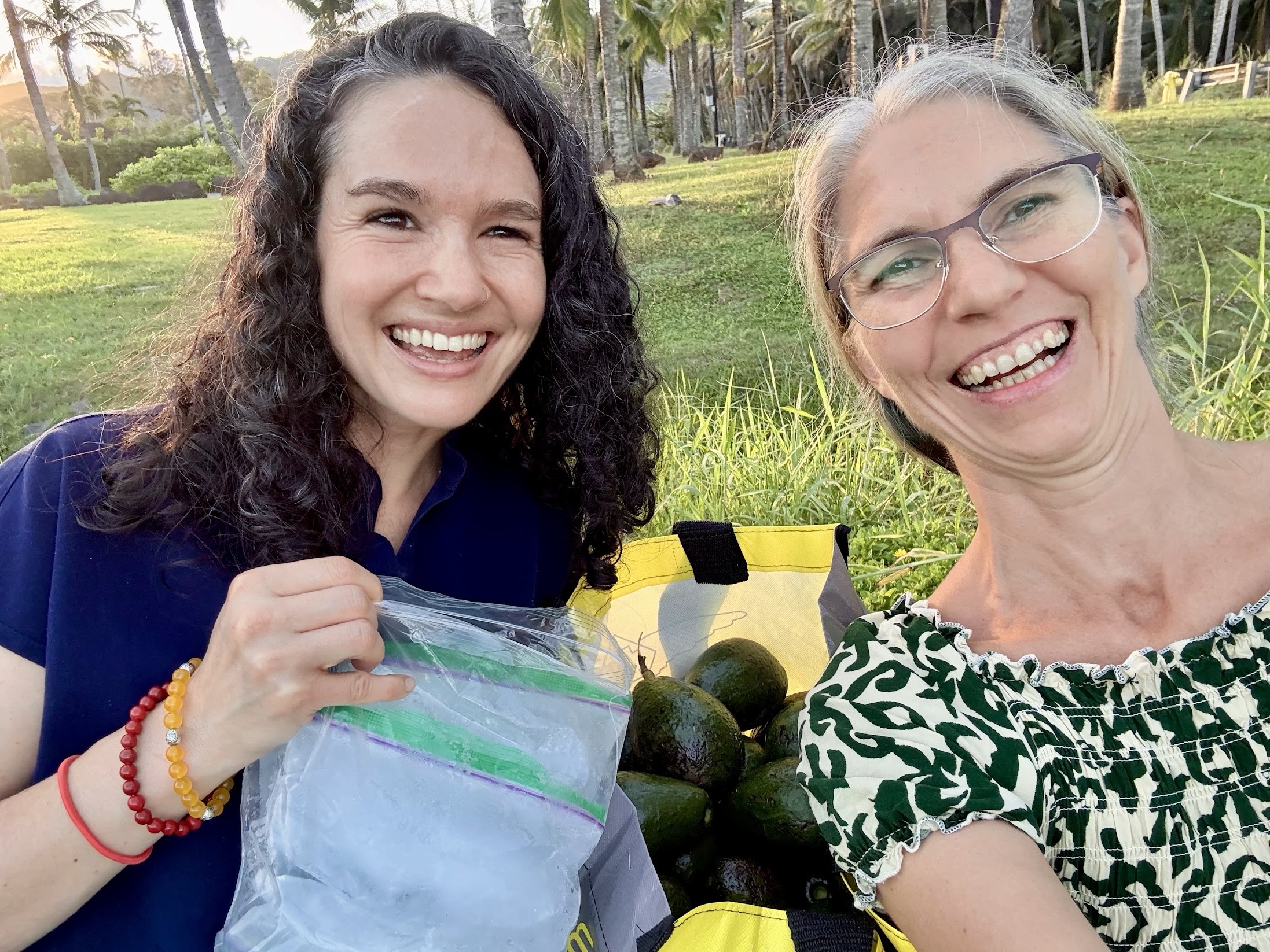 Two Hawaii satsang members smiling outdoors with avocados and a bag of homemade reef-safe sunscreen