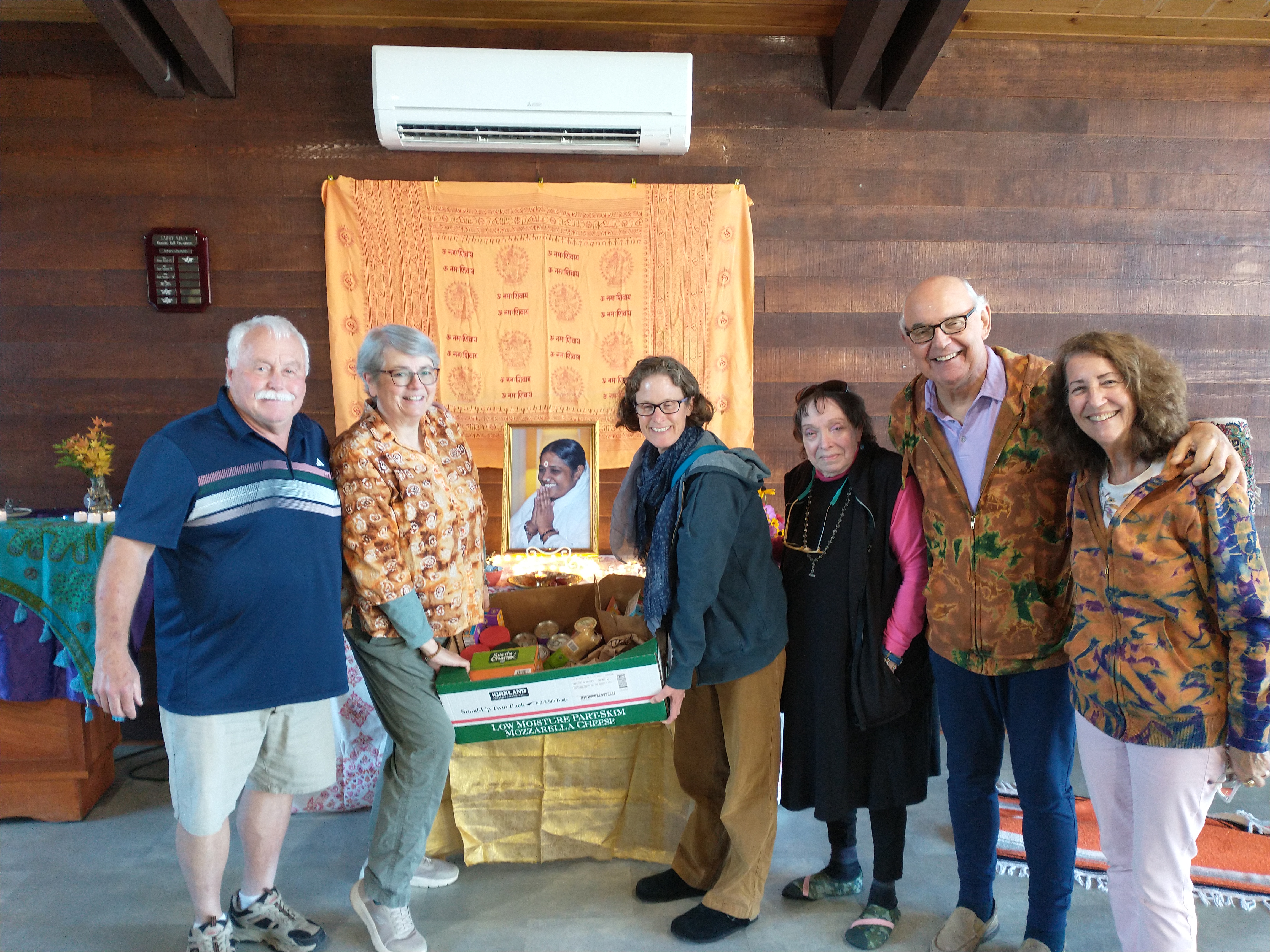 Olympic Peninsula Satsang members holding a box of donated food in front of Amma's picture