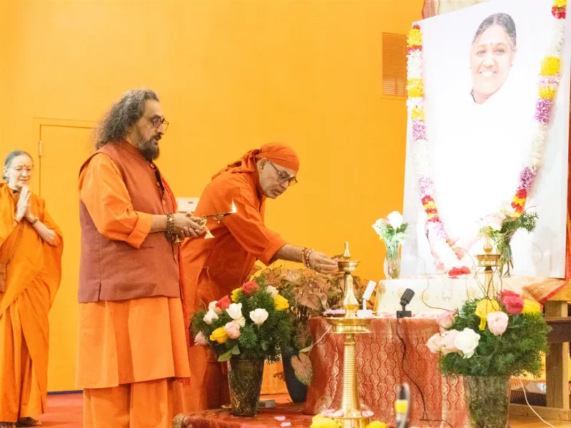 Swamis lighting a lamp before Amma’s portrait