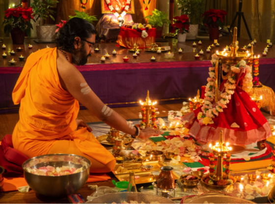 Sarvaishwarya Puja with Swamiji - Sat Jul 1, 5:00 PM Br. Ramanandamrita Chaitanya performing a puja before a lamp covered with a sari and fresh flower garland