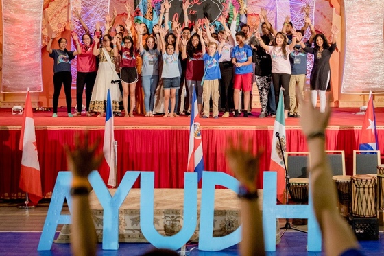 Youth standing with arms raised in front of AYUDH sign
