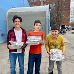 Three young volunteers delivering five trays of cookies from Amma Canada to St Felix Centre